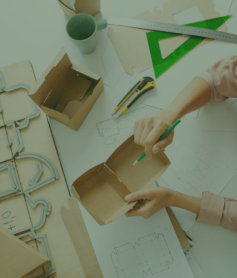Dienstleistung Hintergrund: Hands assembling a cardboard box with pencil, ruler, cutter, and design drawings on a white surface.