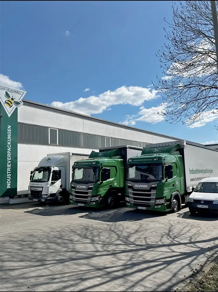 Fahrzeugflotte: Mehrere LKW (Scania, DAF) vor einem Firmengebäude mit dem Logo Wilhelm Hummel Industrieverpackungen.
