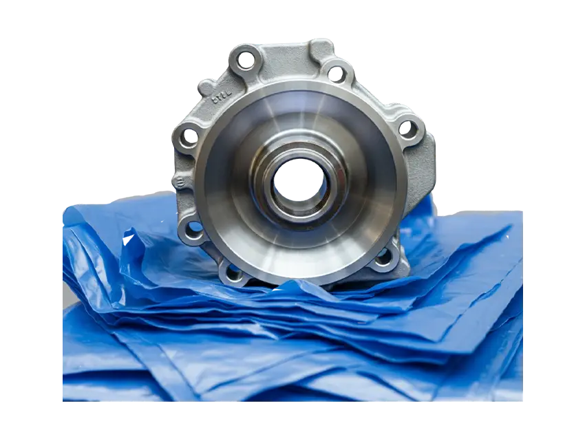 Silbernes Metallbauteil auf blauer Korrosionsschutz-Schlauchfolie. Das Bauteil hat mehrere Öffnungen und eine glatte, runde Oberfläche.