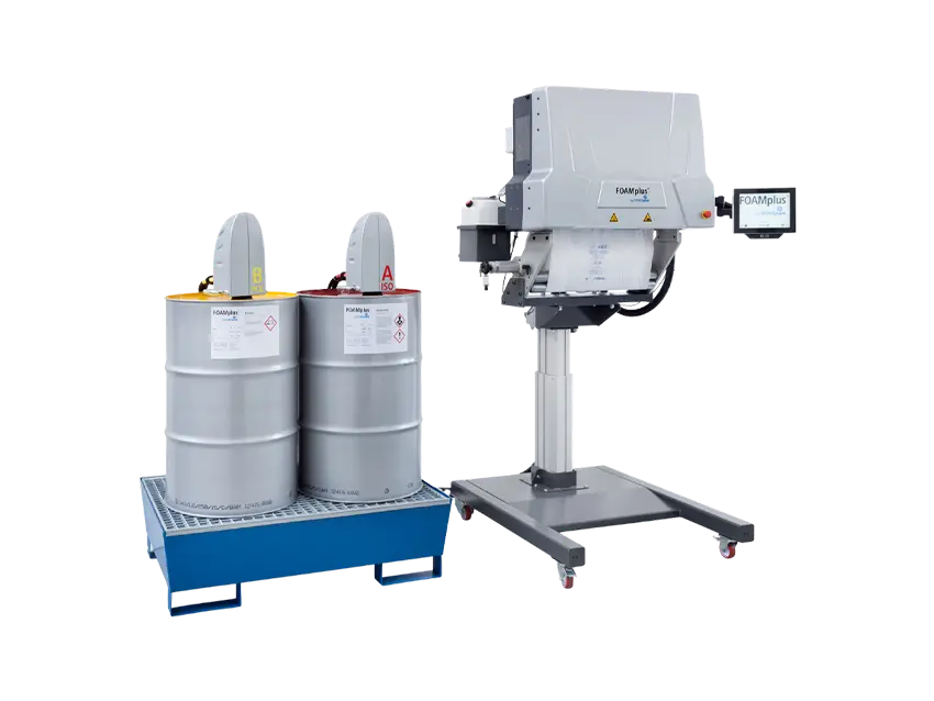 Schutz-Polstersysteme FOAMplus Bag Packer Schaumpolstermaschine: Zwei Fässer auf einer Auffangwanne neben einer Schaumpolstermaschine.